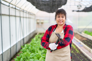 A Smiling woman farmer hold shoveling fork portrait in greenhouse of organic farm