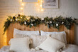 Decoration with spruce branches and garlands headboard of a wooden bed. Christmas chalet style bedroom interior.