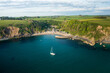 © AmazingAerialAgency - Aerial view of Yacht anchored in Polkerris harbour with view of harbour, beach and surrounding countryside, Par, Polkerris, Cornwall, United Kingdom.
