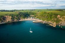 Aerial View Of Yacht Anchored In Polkerris Harbour With View Of Harbour, Beach And Surrounding Countryside, Par, Polkerris, Cornwall, United Kingdom.