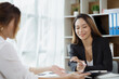 © kamiphotos - Atmosphere in the office of a startup company, two female employees are discussing, brainstorming ideas to working on summaries and marketing plans to increase sales and prepare reports to managers.