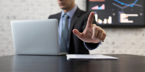 Close-up photo of male hand pointing index finger. Businessman in black suit sitting at the desk and working on laptop in modern office