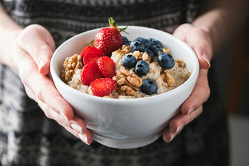 Wall Mural - Oatmeal porridge bowl with berries in female hands. Vegan food, clean eating, dieting concept. Woman's health