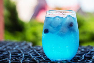 Wall Mural - Glass of tasty blue cocktail and yellow lemons on blured background..Alcohol juicy fruit blue cocktail with curacao liquor, ice cubes and blueberry in frozen glass