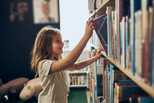 Schoolgirl Choosing Book In School Library. Smart Girl Selecting Literature For Reading. Learning From Books. Benefits Of Everyday Reading. Child Curiosity. Back To School