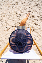 Wall Mural - Woman relaxing on beach reading book sitting on sunbed

