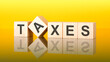 © Maks_Lab - word TAXES made with wood blocks. text is written in black letters and is reflected in the mirror surface of the table, yellow background