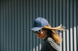 © Cavan Images - a girl in a cap and sunglasses smiles against a gray ribbed wall