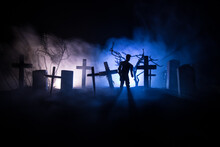 Scary View Of Zombies At Cemetery Dead Tree, Moon, Church And Spooky Cloudy Sky With Fog, Horror Halloween Concept With Glowing Pumpkin. Selective Focus