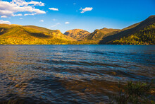 Panoramic View Of Mountain Range By The Lake In Colorado, USA, At Sunset; Waves In Foreground And Blue Sky In Background