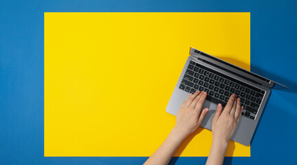 Female hands and laptop on yellow - blue background