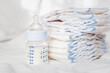 Baby bottle with milk and diapers on a white fabric background. Baby care. First days of life. Feeding and motherhood