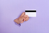 Fototapeta  - Closeup of human's hand holds an empty black business credit card, breaking through purple paper wall, copy space for advertisement or promotion.