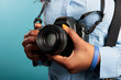 © DC Studio - Close up of professional photographer with photo camera getting ready for shooting session. African american young adult woman having modern DSLR device while standing on blue background.