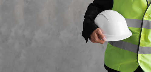 Close-up workwear and helmet in engineer or constructor hand as safety uniform isolated on grey background. Banner