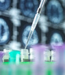 © Connect Images - Close-up of pipette and test tubs in front of brain scans