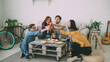 © silverkblack - Happy friends have party talking and eating pizza. They clink bottles sitting on sofa at home indoors