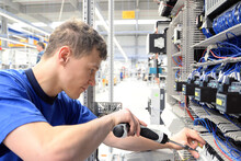Young Apprentice Assembles Components And Cables In A Factory In A Switch Cabinet - Workplace Industry With Future