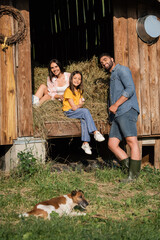 Sticker - happy couple looking at camera near haystack in barn and dog on foreground.