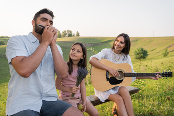 Sticker - man playing harmonica near wife with guitar and happy child in countryside.