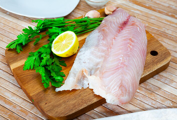 Raw fish with condiments, perch fillet with garlic, parsley and lemon on wooden table