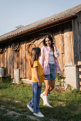 Wall Mural - full length of smiling woman talking to daughter on farm in countryside.