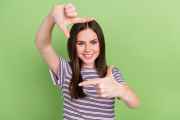 Wall Mural - Portrait of attractive cheerful brown-haired girl showing frame posing isolated over bright green color background