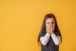 © skif - portrait of a cute little girl covering her mouth with both hands stands on yellow background. The child doesn't want to talk. Keeps a secret, learned a secret