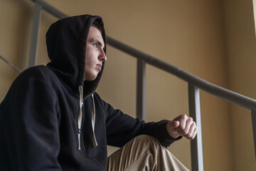 Wall Mural - upset tense young man in a hood, sitting on the stairs and looking away, experiencing problems and misunderstanding. Teenage transition age. The concept of loneliness. Close-up