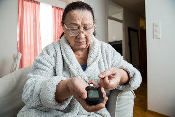 Senior woman checking blood sugar level using home glucometer. Old person with diabetes at home in living room.. Diabetes treatment for elderly people. 