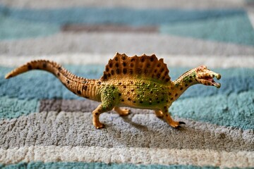 Wall Mural - Closeup shot of a mini spinosaurus toy figure on the carpet floor with blurred background