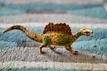 Sticker - Closeup shot of a mini spinosaurus toy figure on the carpet floor with blurred background