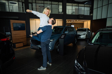 Happy caucasian couple hugging while buying a new car in a car dealership.