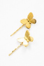 Vertical Shot Of Golden Bobby Pins With Butterfly Decorations On A White Background