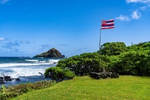 State Flag Of Hawaii At The Seashore With Alau Island Bird Sanctuary In The Background, Maui, Hawaii