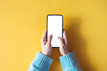 Wall Mural - Close up hand holding black smartphone with white screen on yellow background. Mobile phone frameless design concept.