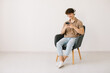 © anatoliycherkas - Attractive young man using laptop, wearing headphones while sitting in armchair against white wall, copy space. Millennial male communicating online or relaxing