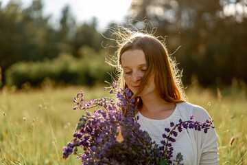 Close up portrait of young beautiful redhead woman with freckles, wearing white dress, posing in the nature. Girl with red hair holding flowers. Natural beauty. Diversity, individual uniqueness.