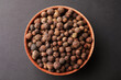 Bowl of allspice pepper grains on grey background, top view