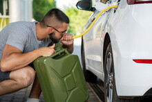A young man steals gasoline from the gas tank in the white car. A young man pumps gasoline from a gas tank into a canister. Fuel and oil crisis. The concept of gasoline prices and the oil crisis.