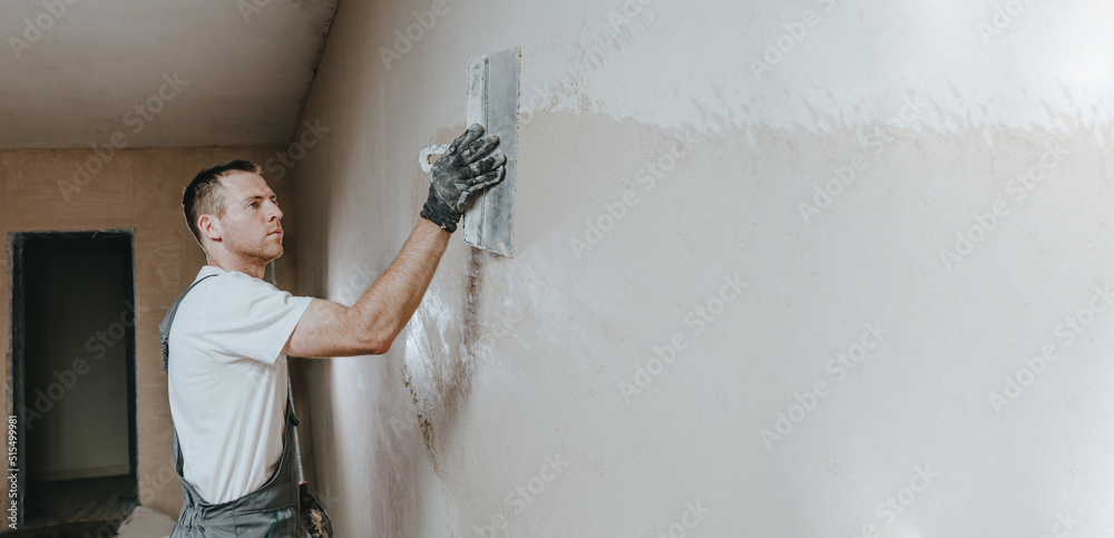 Builder in work overalls plastering a wall indoor