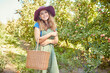 © Jade M/peopleimages.com - Portrait of a woman picking apples from a tree on a sunny day. A young happy female farmer with a basket wearing a stylish straw hat and dungaree on an agricultural farm during harvesting season