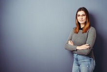 Young Woman With Glasses And Folded Arms Looks At Camera, Blue Wall With Copy Space