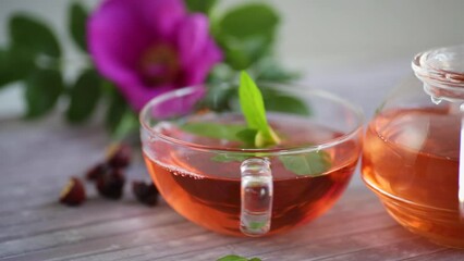 Wall Mural - brewed rosehip tea in a glass teapot with rosehip flowers and mint, on a wooden table.