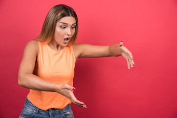 Wall Mural - Pretty young woman holding empty space on palm and looking front on red background