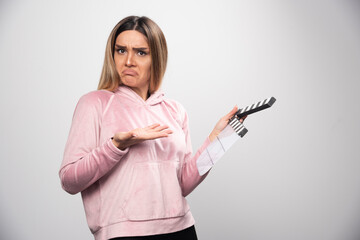 Wall Mural - Blond lady in pink sweatshirt holding a blank clapper board and trying to understand what is it