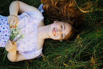 redhead portrait of a beautiful young sexy red-haired woman, lying in the spring sun, relaxing on the green grass.