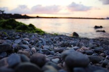 Selective Focus Shot Of Pebble Stones On The Background Of The Body Of Water During Sunset
