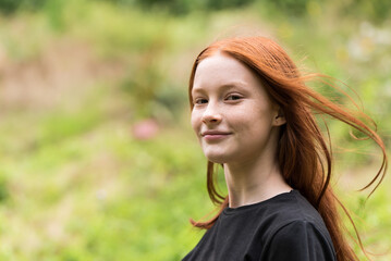 Red haired twelve year old girl with freckles posing with a nature bokeh background