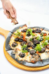 Poster - Vertical closeup of a delicious cuttlefish sausage pizza on a wooden board